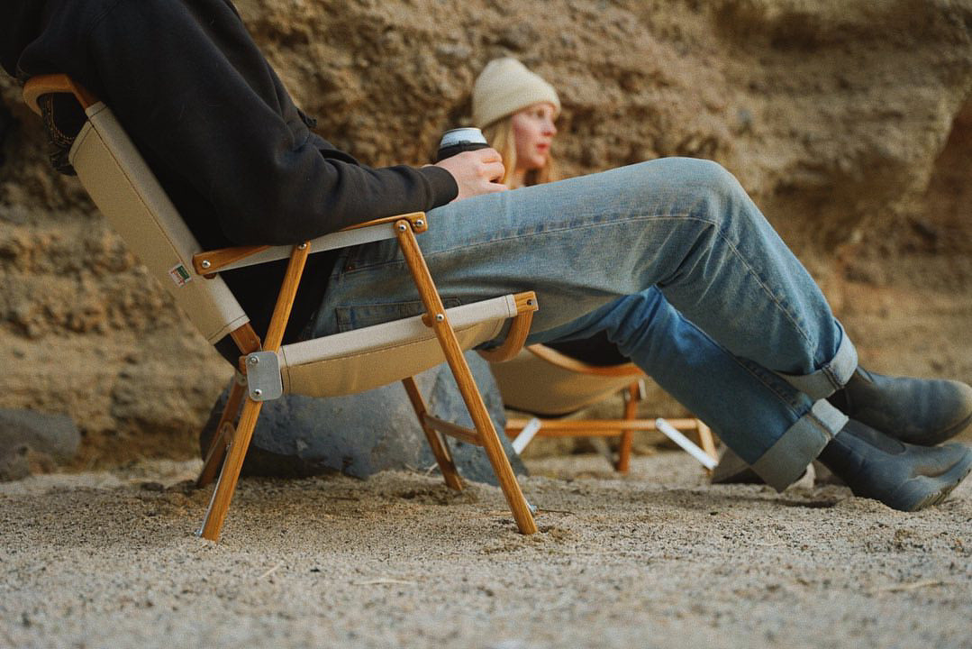 Two people relaxing on their Classic Oak Folding Kermit Chairs made of American white oak enjoying a drink.