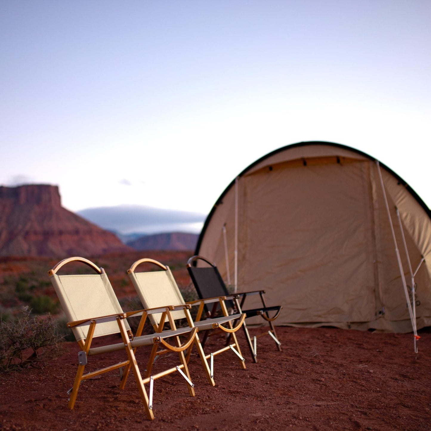 Square cropped three kermit chairs in oak and walnut in oyster and black fabric in front of a tent in the desert camping chairs handmade wooden furniture glamping